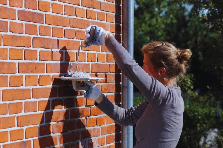 A woman doing tuckpointing on a brick chimney.