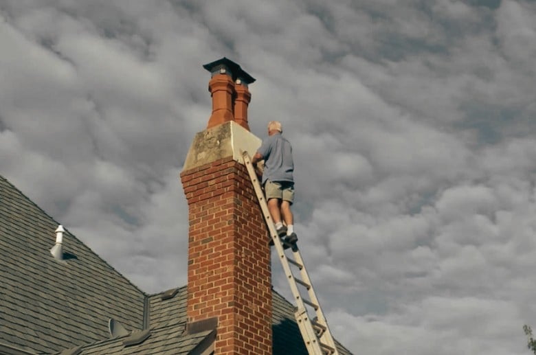 A man on a ladder leaning on a chimney.