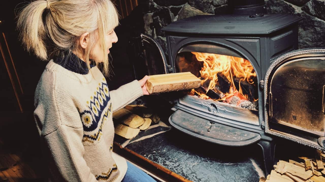 A woman burning firewood in a wood stove. Find out - is it legal to burn wood in a fireplace in California.