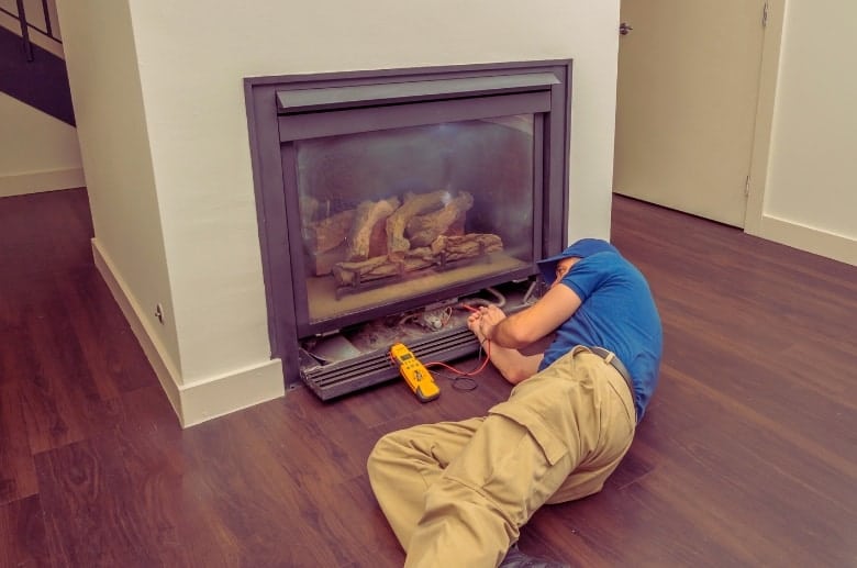 A fireplace technician cleaning a gas fireplace. The maintenance is one of the things to consider when comparing Vented vs Ventless Gas Fireplaces.