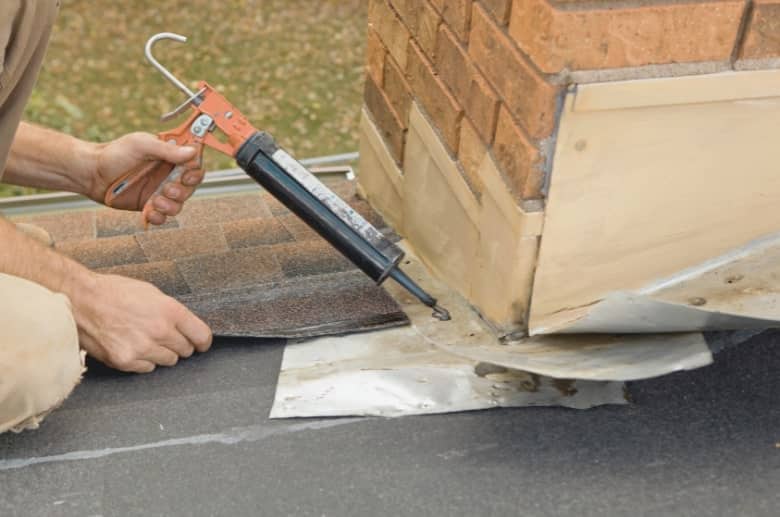 A technician is applying sealant on a chimney flashing. These are the tools needed on How to Fix a Chimney Flashing Leak.