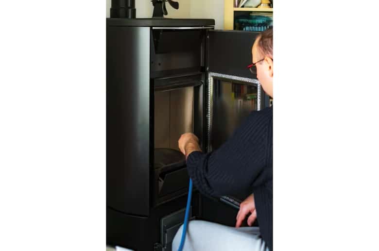 Man cleaning a pellet stove with a vacuum. It is part of the Pellet Stove Maintenance.