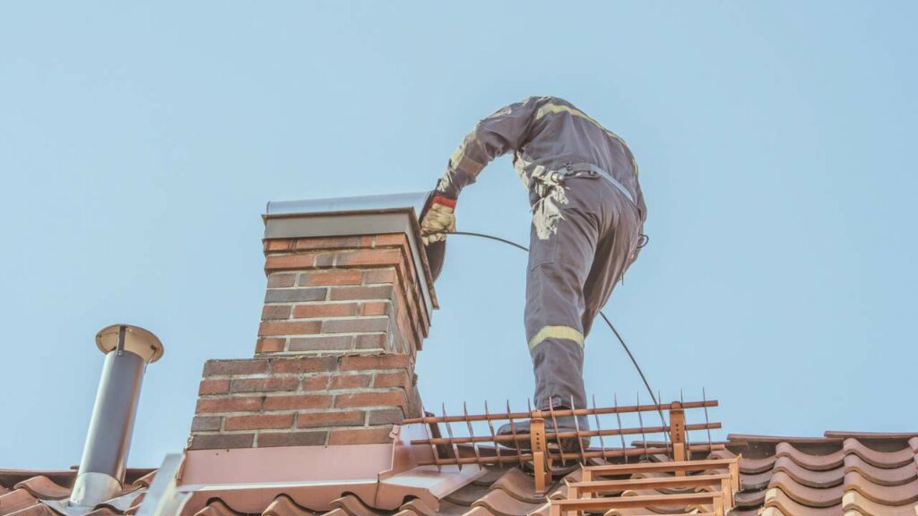 A technician doing a chimney sweep on the roof. What Is Included in a chimney sweep? Find out more.