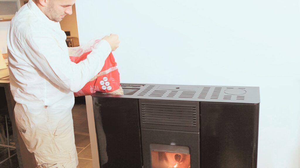 A man pouring pellets into a pellet stove. Know the answer to your question "why is my pellet stove using so many pellets?".